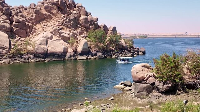 Egyptian scenery on the nile river, with a traditional boat carrying tourists near philae island and the aswan low dam in the background