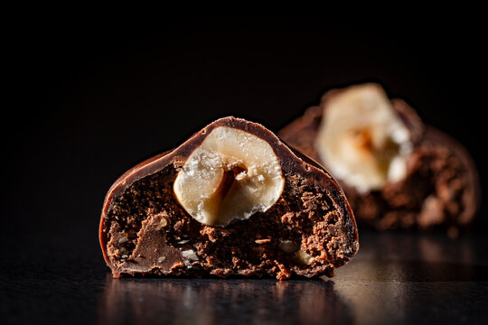 Chocolate truffle with whole hazelnut filling, closeup. Macro of chocolate truffle cut in half revealing whole hazelnut and creamy filling. Premium handcrafted confection on dark background