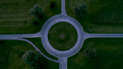 Naklejka premium Aerial view of a modern roundabout surrounded by lush greenery, highlighting its geometric design and smooth traffic flow.