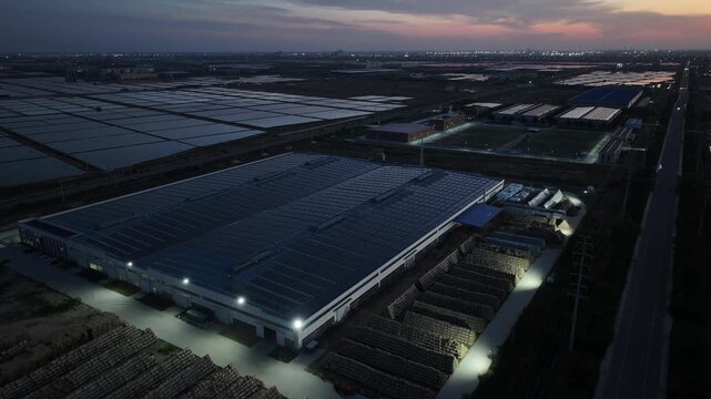 Aerial view of industrial complex at dusk with illuminated warehouses and timber stacks