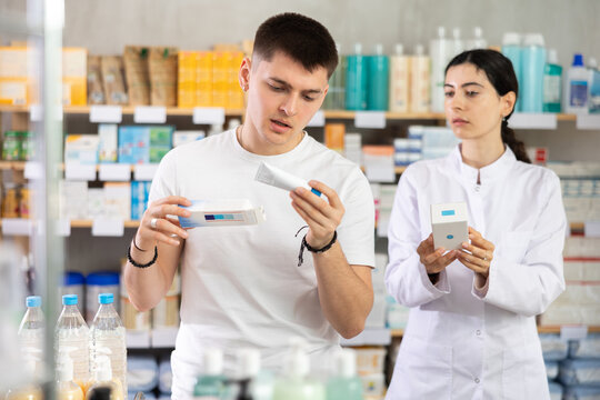 Man chooses ointment or gel in modern pharmacy. Female pharmacist helps with choosing a medicine