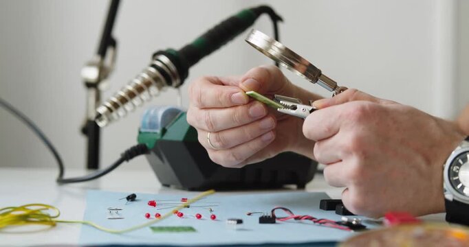 Close-up of Technician Hands Repairing Electronics with Precision Tools, Magnifying Glass, and Soldering Station on Workbench