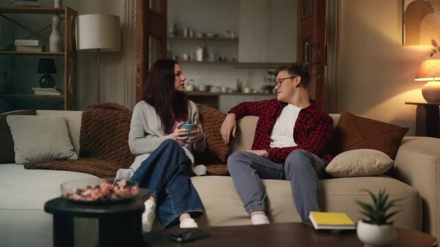 Happy teen son and his mother talking while relaxing on the couch, family time