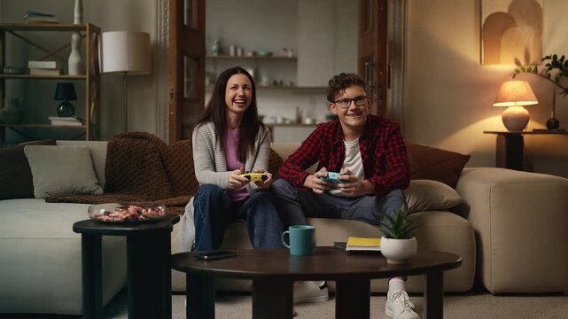 Excited mom and teen son playing video games together, enjoying family time