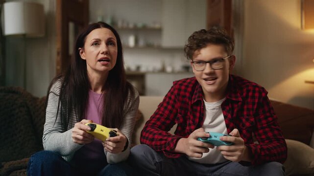 Happy teen son and his mom playing video games with gamepads, family hobby