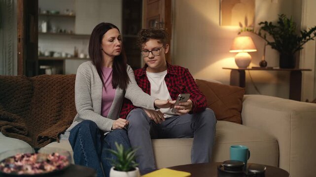 Mother asking her adolescent son about a new mobile app, browsing phone together