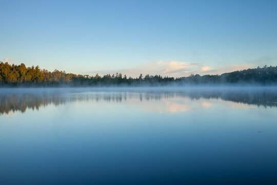 Morning fog on a blue northern Minnesota lake with pines on the shore under blue sky