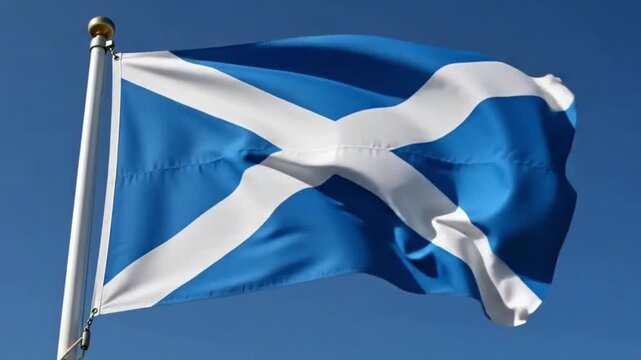 The national flag of scotland, the saltire, featuring a white diagonal cross on a blue field, waving against a clear blue sky
