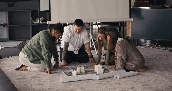 A group of four people gathers around a table to discuss and build models, sharing ideas and plans in a workspace