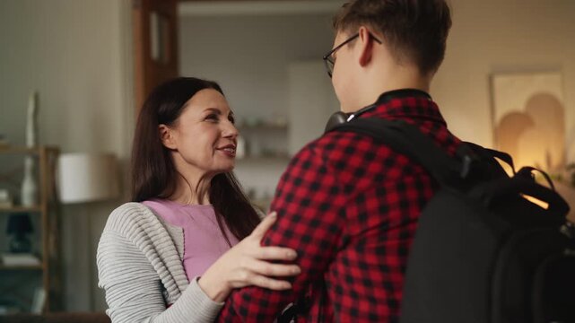 Smiling mother embracing her adolescent son returning home from college, reunion