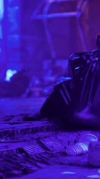 A pile of trash is on the street surrounded by scattered items. Purple lighting gives a unique look to the scene. It is night and the area appears messy and unkempt.