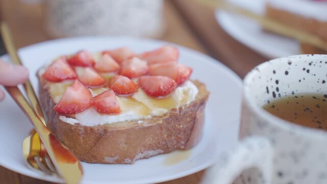 Hand sets French toast plate on table and places fork and knife beside toast. Concept of breakfast serving and homemade brunch