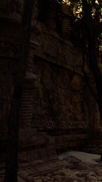 Visitors explore a historical site with carved stone walls. A tree stands in the area, adding to the atmosphere. The carvings show detailed designs and figures from the past.