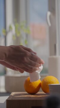 Person dries orange with paper towel near kitchen window, with oranges on wooden board. Concept of citrus preparation and clean fruit