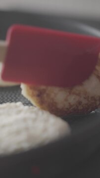 Cottage cheese pancake is flipped in frying pan with spatula while other pancakes cook nearby. Concept of homemade breakfast and simple dairy recipe