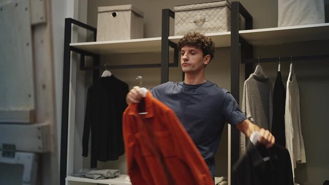 Young man choosing jackets in front of mirror, getting ready to leave home