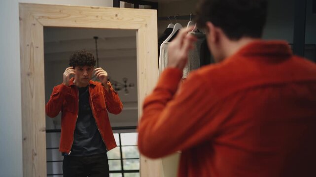 Attractive young man in trendy orange jacket posing by mirror, self-confidence