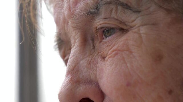 Close up profile view of elderly caucasian woman face. Highlighting wrinkled skin around her eyes as she looks off screen with thoughtful expression. Eyelid twitches due to tremor or Parkinson disease