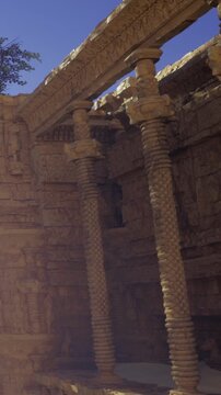 Visitors explore the ruins of an ancient structure in India. Stone pillars show detailed carvings. The sun shines brightly, highlighting the craftsmanship of the architecture.