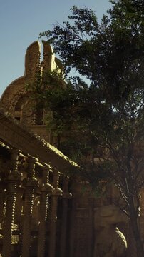 Visitors walk around a historic temple as the sun sets. The detailed carvings on the stone and green trees surround the site. People admire the structure and take pictures of the surroundings.
