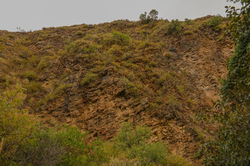 Rocky cliff slope with sparse vegetation and dry mountain terrain under cloudy sky © GraysonStock