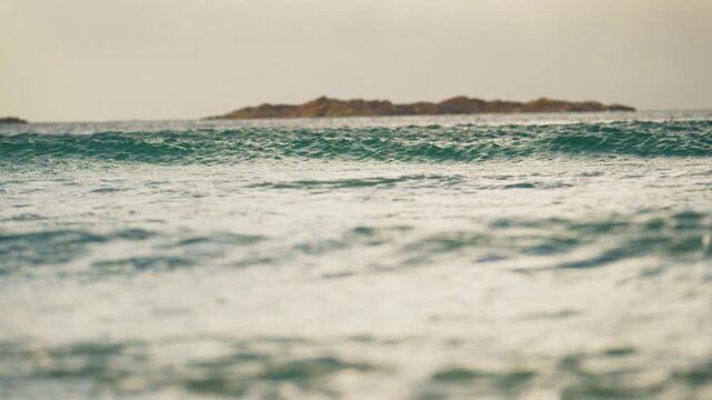 Soft ocean surf with distant rocky island in peaceful coastal light