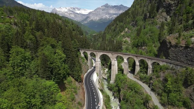 Aerial view of the historic stone railway viaduct crossing a dramatic alpine gorge with mountain road and snow-covered peaks near Chamonix in the French Alps