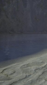 A person stands near the riverbank with water flowing beside them. The scene shows the sandy shore and rocky cliffs in the background. The sunlight brightens the area around them.