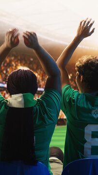 Vertical video: Rear view of football supporters starting crowd wave across packed stadium rows during match for goal celebration, supporter emotion and fan culture content.