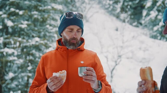 Hiker with beard takes break eating bread and drinking in snowy forest