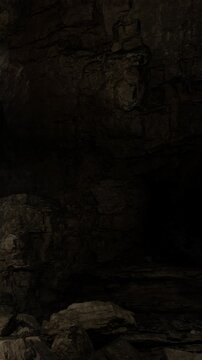 In a dark cave, people explore rocky walls and hidden passages. Light barely reaches the ground as they navigate through the uneven surfaces and twists of the cave.