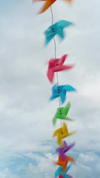 Multicolored pinwheels spinning on string against cloudy sky. Vertical row of multicolored plastic pinwheels blurred by motion against a pale cloudy sky.