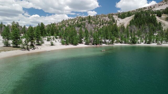 Sunny Summer Drone Flight Over Turquoise Mountain Lake with Snow and Pine Trees