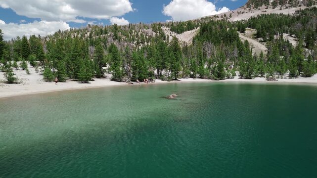 Sunny Summer Drone Flight Over Turquoise Mountain Lake with Snow and Pine Trees