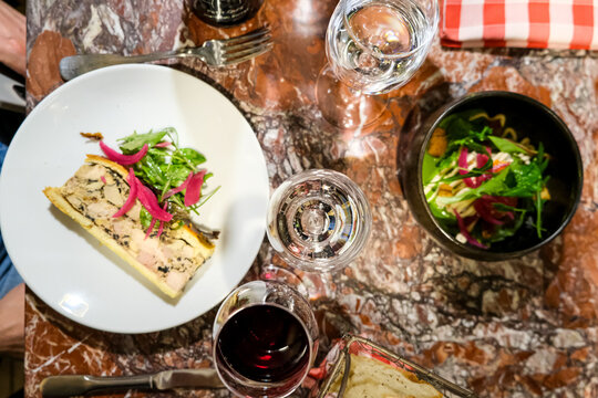 A slice of artisanal P&acirc;t&eacute; en Cro&ucirc;te and a skate wing ceviche salad served with red wine on a marble table at a traditional Lyonnaise bouchon. This top-down overhead flat lay captures the gourmet Frenc