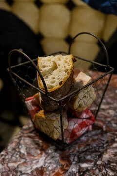 Slices of rustic French sourdough baguette served in a dark wire basket on a marbled restaurant table. This close-up shot focuses on a freshly cut slice of bread highlighting its thick, crispy golden 