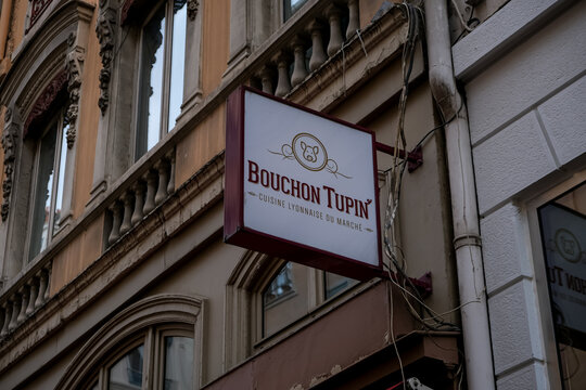 Lyon, France - 10.03.2026. A low-angle medium shot of the hanging outdoor business sign for "Bouchon Tupin," a traditional restaurant in Lyon, France. The white rectangular sign features the restauran