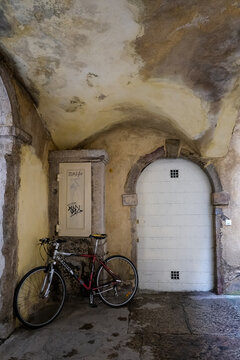 Lyon, France - 10.03.2026. A classic stone courtyard interior featuring an MBK mountain bike parked next to an old, weathered plaster wall, an arched white wooden service door with small metal grilles