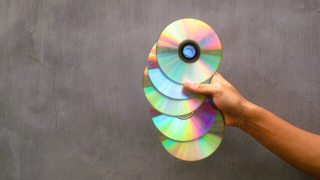 A hand holding a stack of shiny reflective vintage compact discs against a grey background.