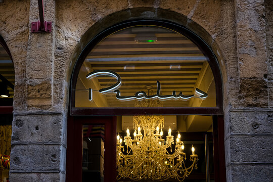Lyon, France - 10.03.2026. A close-up shot of the famous Pralus bakery and chocolate shop storefront in Lyon, featuring a luminous white script neon sign set within an arched window, showcasing a larg