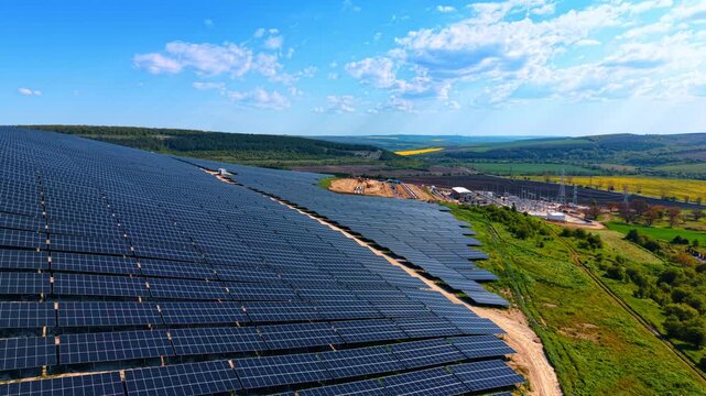 Solar farm and grid substation across rural hills, blue arrays border dirt tracks and forested fields.