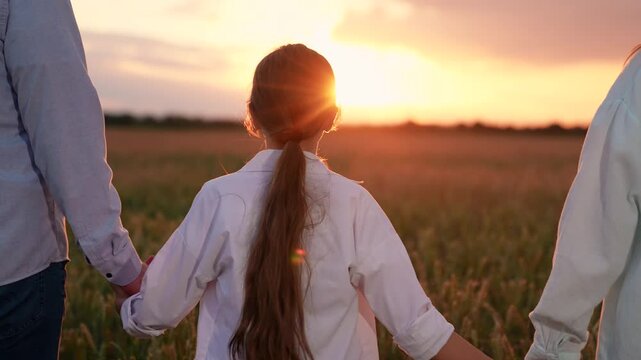 Child daughter, dad mom walk hand in hand in wheat field sunset, close-up. Happy farming family with child strolls wheat field. Farmers father mother young daughter enjoy nature together outdoors, sky