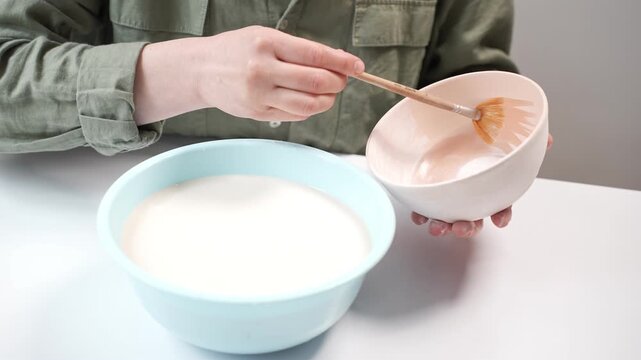 artist applying thick glaze to bisque pottery. Ceramicist using a broad paintbrush to glaze a handmade clay bowl 4k footage