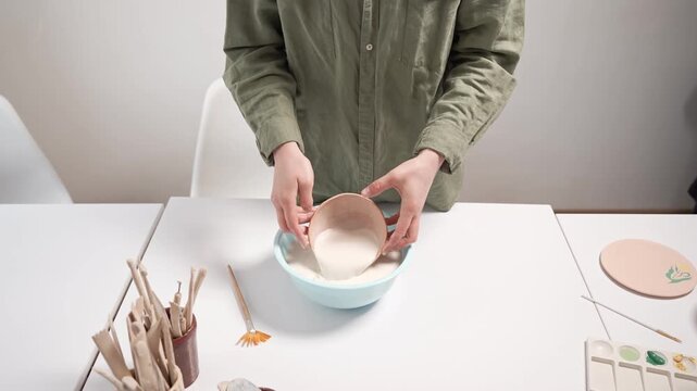 Artisan dipping a ceramic bowl into a large glaze basin in a professional 4k video. The craftsperson carefully handles an unglazed clay vessel during the traditional manual glazing process