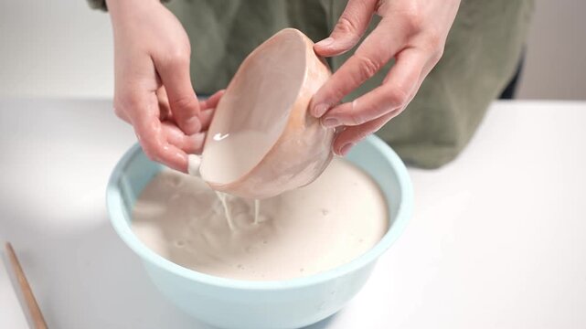 4k video showing an artisan dipping a raw ceramic bowl into a liquid glaze basin. Potter handles the unglazed clay vessel to ensure an even coating during the manual production process