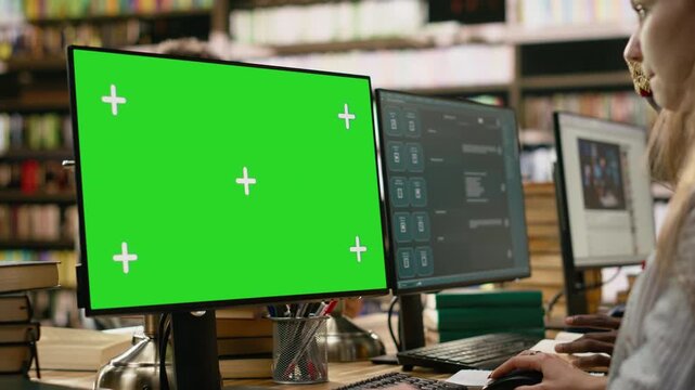 Green screen mockup on desktop near student at shared library table with peers, computer class with people using monitors, for education technology.