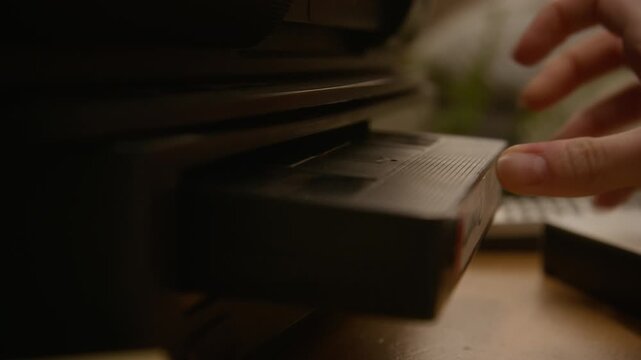 Caucasian female hand inserting VHS tape labeled Zombie Attack 5 into VCR player. Footage serves retro technology, nostalgia, or horror movie themed marketing campaigns