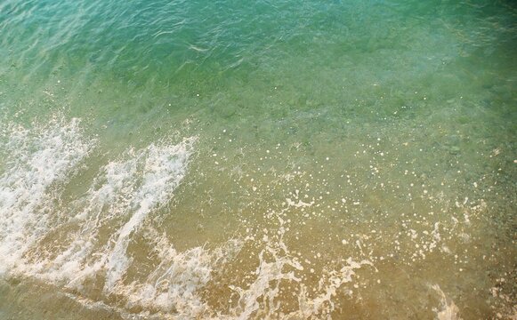 Turquoise sea surface with crushing waves and foam colorful water ariel shot summer sea background
