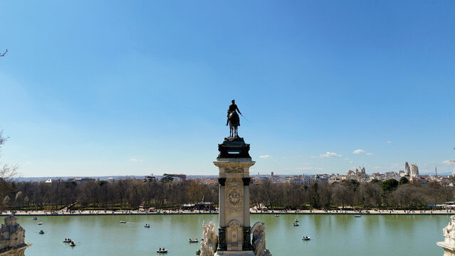Drone view of the Monument to Alfonso XII overlooking the boating lake in El Retiro Park with the Madrid skyline in the background. Clear spring day with large copy space in the sky