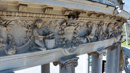 Close-up of an elaborate decorative stone relief featuring cherubs, floral motifs and heraldic elements on the colonnade of the Monument to Alfonso XII in Madrid, Spain © EugeniVisuals